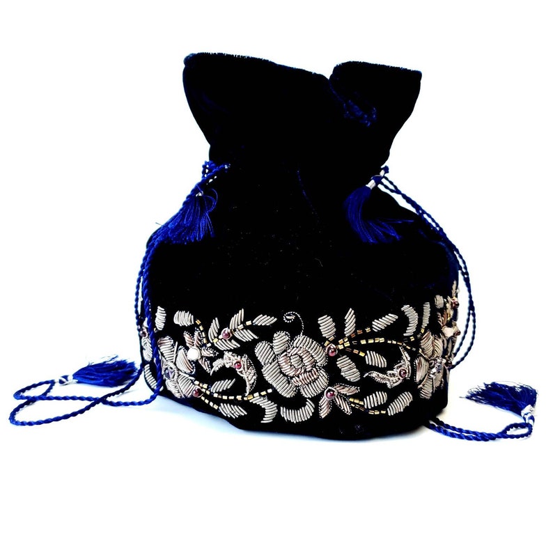 K&ouml;nnte beinhalten: Eine dunkelblaue Samt-Kordeltasche mit einem silbernen und goldenen Blumenstickerei-Design. Die Tasche hat an jeder Seite einen Quasten.