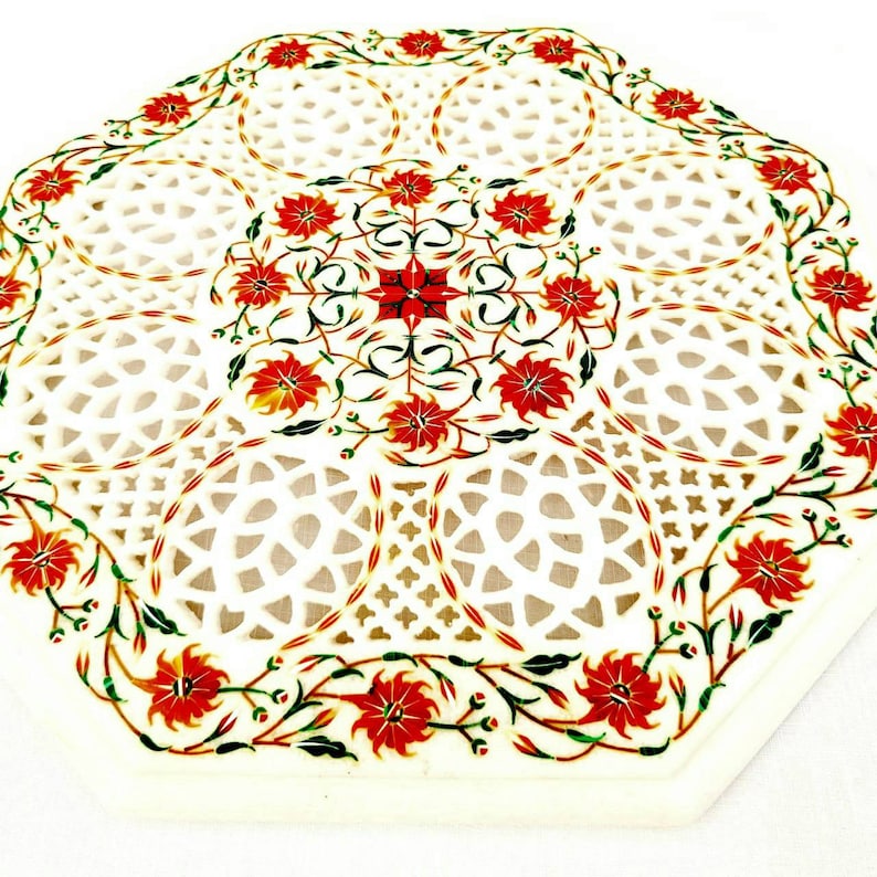 Puede incluir: Tapa de mesa octogonal de m&aacute;rmol blanco con un intrincado dise&ntilde;o de corte y un patr&oacute;n floral rojo.