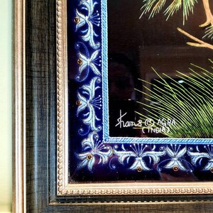 Puede incluir: Una obra de arte enmarcada que presenta un p&aacute;jaro azul posado en una rama con hojas verdes. El marco tiene un borde decorativo con dise&ntilde;os florales azules y blancos. La obra est&aacute; firmada "Khams Agra India".