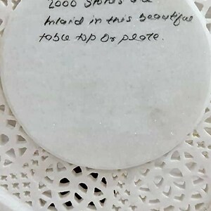 Puede incluir: Un plato de m&aacute;rmol blanco con intrincados recortes. El plato tiene una inscripci&oacute;n circular que dice "2000 Stones are inlaid in this beautiful top of plate."
