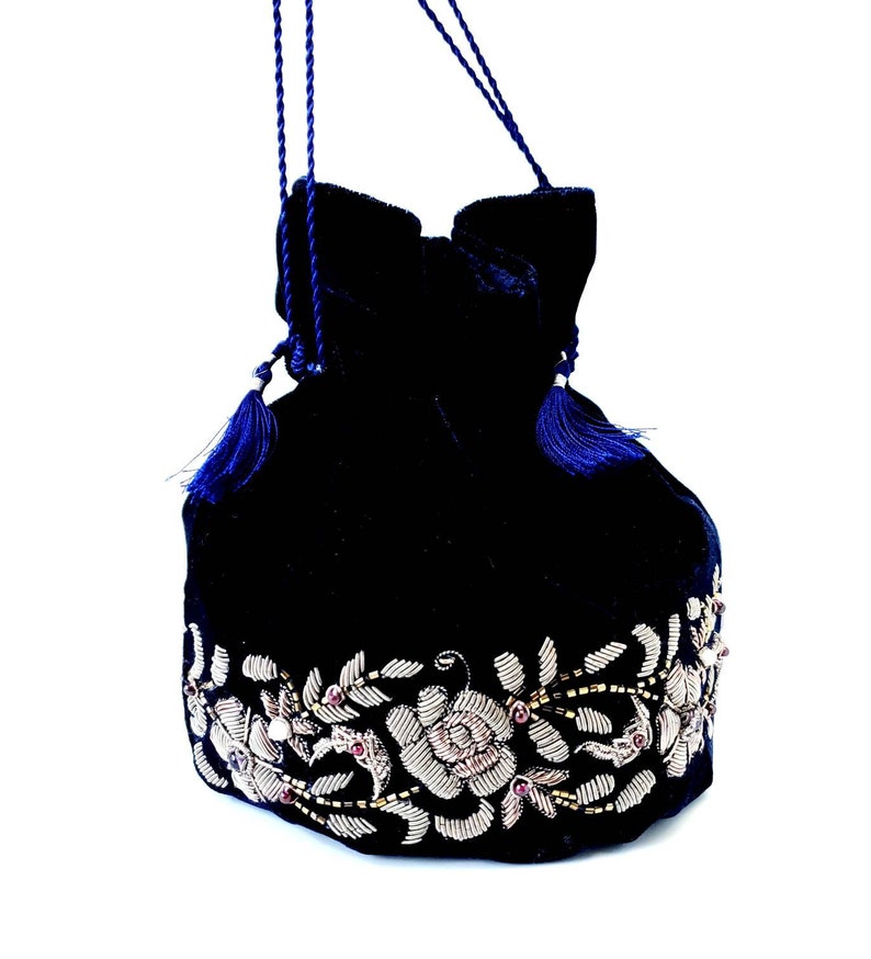 K&ouml;nnte beinhalten: Eine dunkelblaue Samt-Kordeltasche mit einem silbernen und rosafarbenen Blumenstickerei-Design.