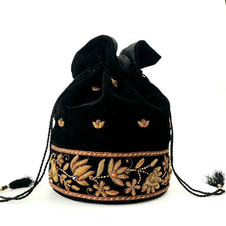 May include: Black velvet drawstring bag with gold embroidery of floral designs and a gold trim. The bag has a black tassel on each side.