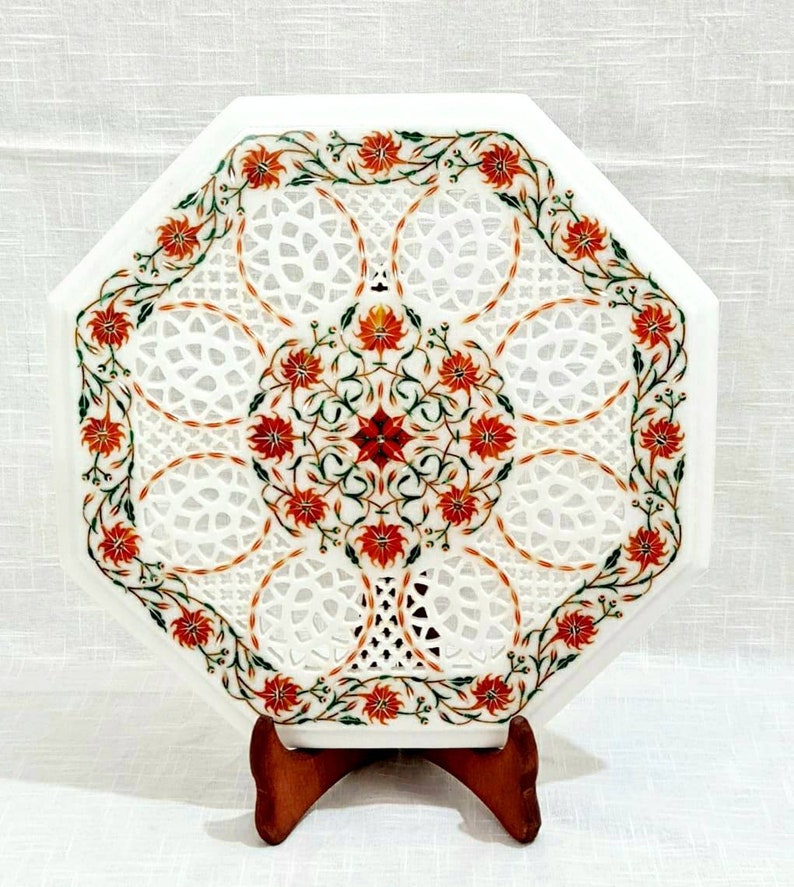 Puede incluir: Mesa de centro octogonal de m&aacute;rmol blanco con intrincados dise&ntilde;os florales y geom&eacute;tricos en rojo, verde y blanco. La mesa de centro est&aacute; sobre un soporte de madera.