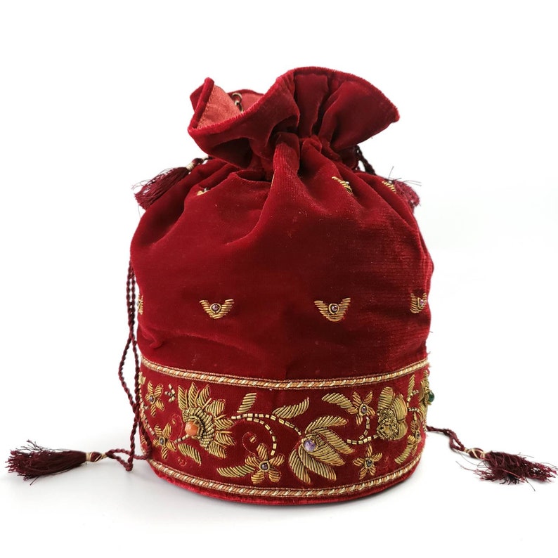 May include: A red velvet drawstring bag with gold embroidery and jewel accents. The bag has a tassel on each side.