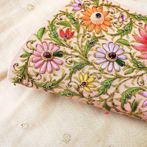 May include: A pink fabric clutch with intricate floral embroidery in shades of pink, green, yellow, and orange. The flowers are embellished with colorful jewels.
