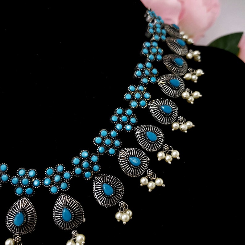 May include: A silver necklace with blue and white stones. The necklace has a teardrop shape and is decorated with small flowers.