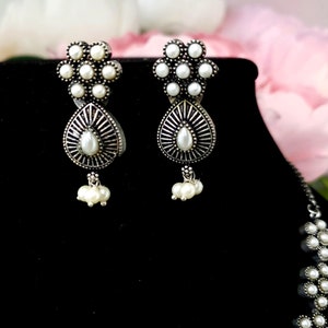 May include: A pair of silver earrings with white pearl accents. The earrings feature a flower design with a teardrop-shaped pendant.