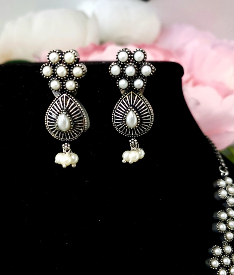 May include: A pair of silver earrings with white pearl accents. The earrings feature a flower design with a teardrop-shaped pendant.