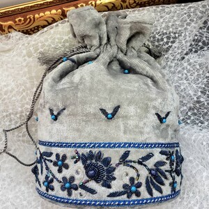 May include: A gray velvet drawstring bag with a blue and silver beaded trim. The bag is decorated with blue beads and silver embroidery.