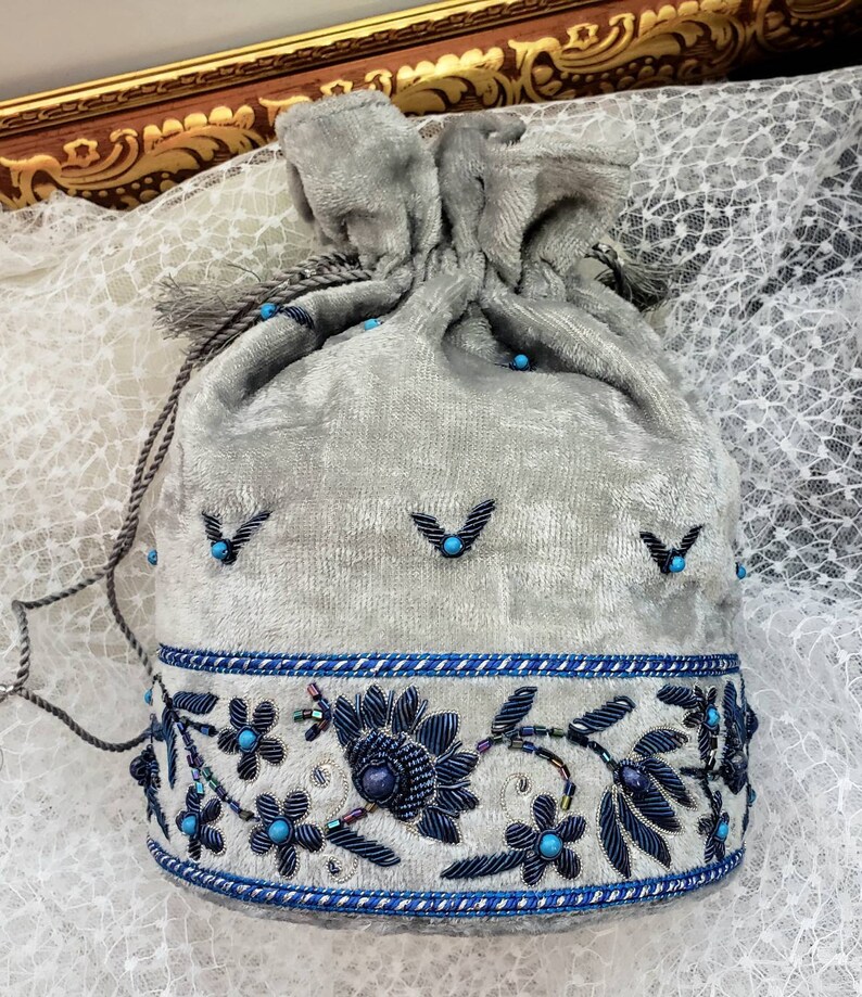 May include: A gray velvet drawstring bag with a blue and silver beaded trim. The bag is decorated with blue beads and silver embroidery.