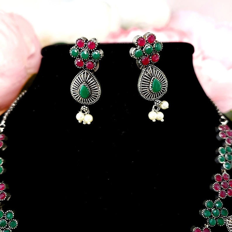 May include: A silver necklace and earrings set with green and pink stones. The necklace has a scalloped design and the earrings have a teardrop shape.