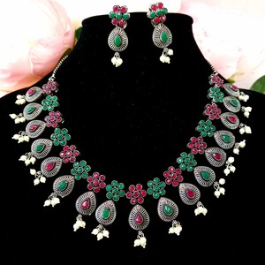 May include: A silver necklace and earrings set with green and pink stones. The necklace features a teardrop design with pearl accents.