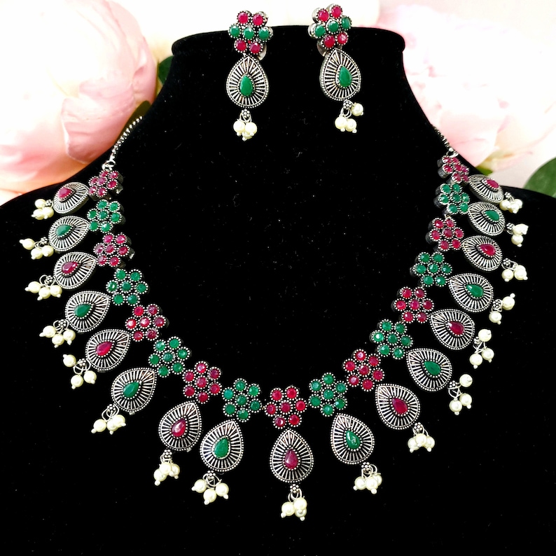 May include: A silver necklace and earrings set with green and pink stones. The necklace features a teardrop design with pearl accents.