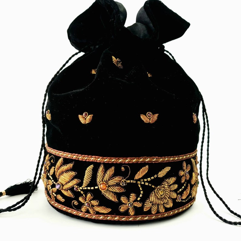 May include: A black velvet drawstring bag with gold embroidery and jewel accents. The bag has a tassel and a floral design around the bottom.