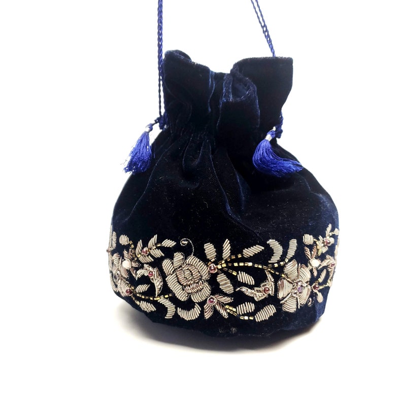 K&ouml;nnte beinhalten: Eine dunkelblaue Samt-Kordeltasche mit einem silbernen floralen Stickmuster. Die Tasche hat an jeder Seite einen blauen Quasten.