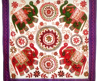 May include: A white fabric wall hanging with a purple border features four embroidered elephants in red and green with intricate floral designs and mirror accents.