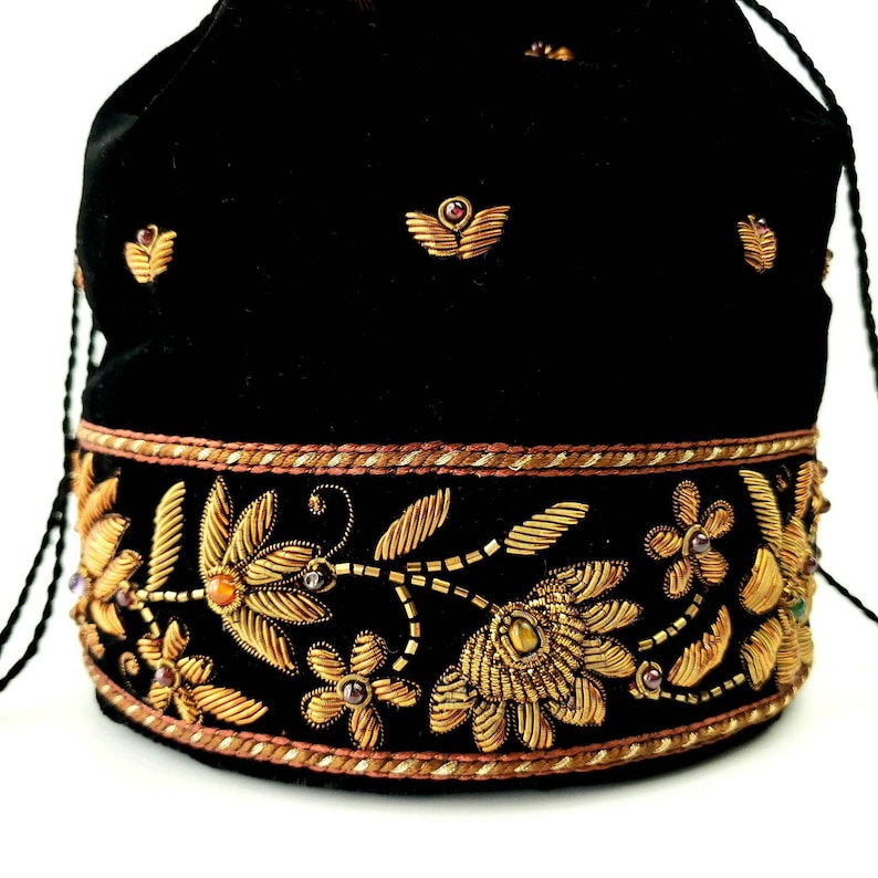 May include: Black velvet drawstring bag with gold embroidery of floral designs and small jewels. The bag has a gold and brown trim.