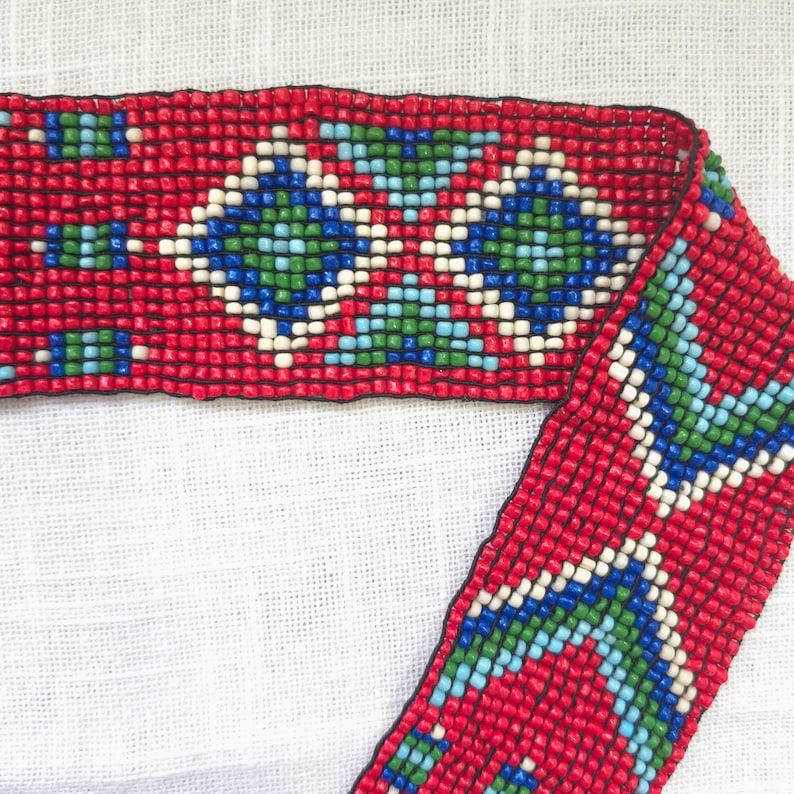 May include: Red beaded trim with a geometric pattern in blue, green, and white. The trim is made of small, square beads.