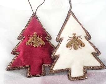 Puede incluir: Dos adornos de árbol de Navidad de fieltro con ribetes dorados y un diseño de abeja bordado en oro. Un árbol es rojo y el otro es blanco.