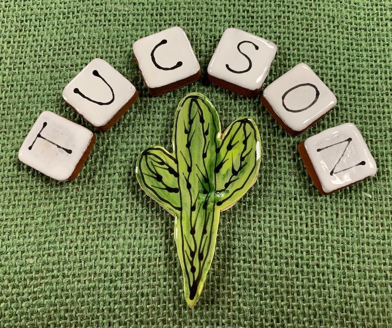 May include: White ceramic tiles spelling out the word "TUCSON" with black lettering, arranged in a semi-circle around a green cactus illustration.