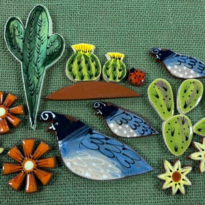 May include: A collection of ceramic mosaic tiles featuring various shapes including a tall green cactus, two round green cacti, two blue and white quail birds, a small red ladybug, orange and yellow flowers, and several light green leaf shapes.