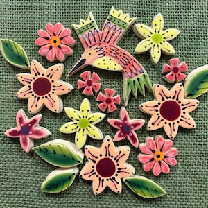 Puede incluir: Una colección de azulejos de mosaico de cerámica que presenta un colibrí central en rosa, amarillo y verde, rodeado de varias formas florales en tonos rosa, melocotón y amarillo, junto con varios azulejos en forma de hoja verde con detalles.