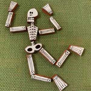 May include: A white ceramic skeleton made of individual pieces, each with black painted details. The skeleton is posed in a playful, almost dancing position.