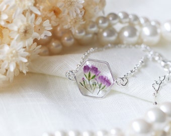 Puede incluir: Un brazalete de cadena de plata con un dije hexagonal de resina transparente con flores moradas prensadas.