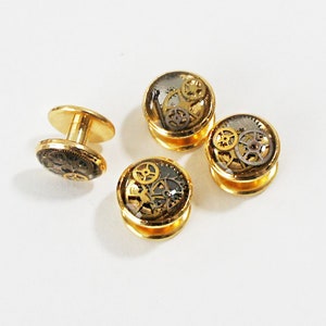 May include: Set of four gold-toned cufflinks with a clear resin top featuring a detailed steampunk design of gears and cogs.