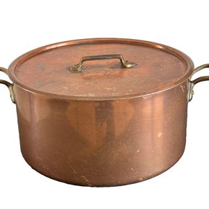 May include: A copper pot with a lid and two brass handles. The pot is round and has a shiny surface.