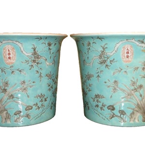 Puede incluir: Un par de macetas de cerámica turquesa con diseños florales y caracteres chinos. Las macetas están decoradas con un patrón floral marrón claro y tienen un borde blanco.