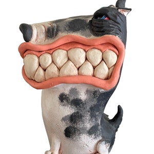 May include: A ceramic sculpture of a dog with a black and white spotted body and a large, open mouth with pink gums and white teeth. The dog has a blue eye and a black nose.