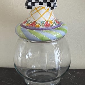 Peut inclure: Un bocal en verre transparent avec un couvercle décoratif. Le couvercle présente un nœud à carreaux noir et blanc, un motif floral et des rayures bleues, vertes et violettes. Le bocal est conçu pour le stockage.