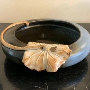 May include: A ceramic bowl with a blue and black glaze. The bowl has a leaf-shaped handle and a decorative leaf design on the side.