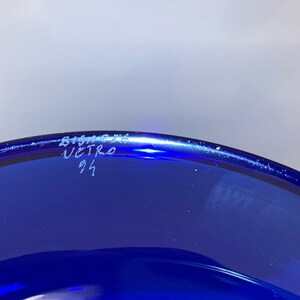 Puede incluir: Primer plano de la parte inferior de un cuenco de vidrio azul cobalto con la inscripci&oacute;n "Bitossi Vetro 91" escrita en blanco.