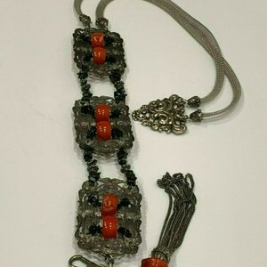 May include: A silver chain necklace with a tassel and three square pendants featuring red and black beads.