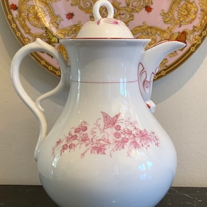 May include: White porcelain coffee pot with a red floral design and a butterfly. The pot has a lid with a knob and a handle.