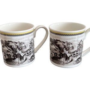 Puede incluir: Dos tazas de cerámica blanca con ilustraciones en blanco y negro de un hombre caminando con un perro en una zona boscosa. Las tazas tienen una banda amarilla alrededor de la parte superior.