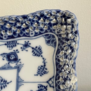 May include: A white ceramic square serving dish with a blue and white floral pattern and a decorative lace-like border.