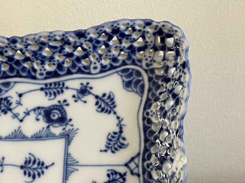 May include: A white ceramic square serving dish with a blue and white floral pattern and a decorative lace-like border.