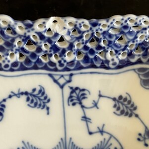 May include: A white porcelain plate with a blue and white floral pattern. The plate has a scalloped edge with a delicate openwork design.