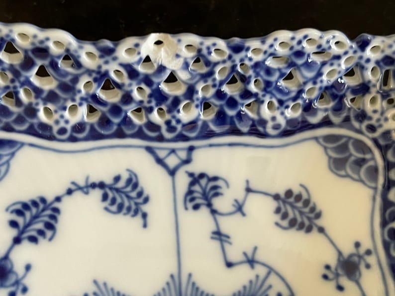May include: A white porcelain plate with a blue and white floral pattern. The plate has a scalloped edge with a delicate openwork design.
