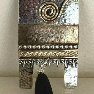 Peut inclure: Un pendentif en argent et or avec une goutte de pierre noire. Le pendentif présente un design texturé et un détail de fil en spirale.