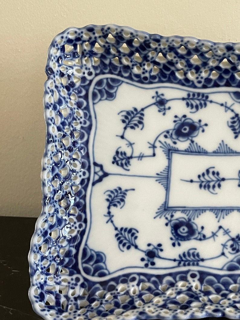 May include: A square blue and white porcelain serving tray with a delicate openwork lace design around the edge. The tray features a traditional blue and white floral pattern.
