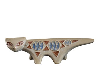 Może przedstawiać: Ceramiczna figurka kota o stylizowanym wzorze. Kot jest jasnoszary z brązowymi i niebieskimi wzorami geometrycznymi.