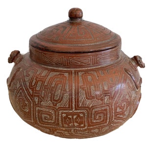 May include: A brown ceramic pot with a lid, decorated with intricate geometric patterns. The pot has two handles on the sides and a rounded body.