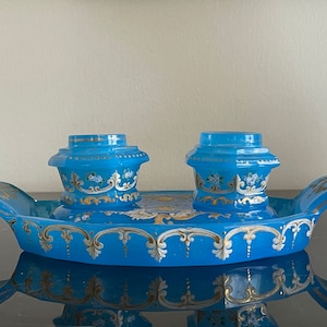 Puede incluir: Un juego de tintero de vidrio azul con dos tinteros y una bandeja. Los tinteros y la bandeja están decorados con diseños florales dorados y blancos.