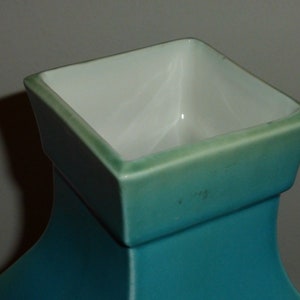 Pode incluir: Um vaso de cer&acirc;mica turquesa com uma abertura quadrada. O vaso tem um acabamento esmaltado e uma superf&iacute;cie lisa.