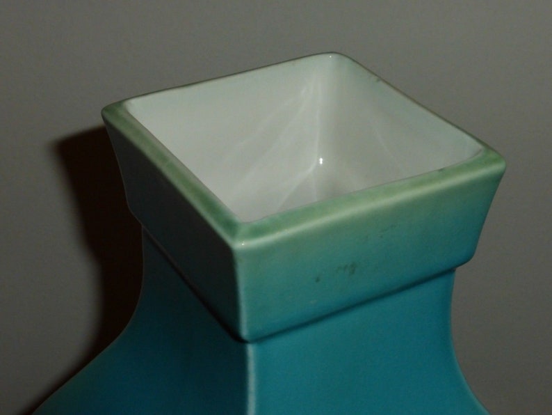 Pode incluir: Um vaso de cer&acirc;mica turquesa com uma abertura quadrada. O vaso tem um acabamento esmaltado e uma superf&iacute;cie lisa.