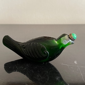 May include: A green glass bird-shaped bottle with a jade green stopper. The bottle has a detailed design and is a vintage piece.